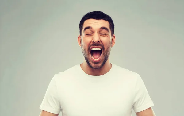 Gek schreeuwen man in t-shirt over grijze achtergrond — Stockfoto