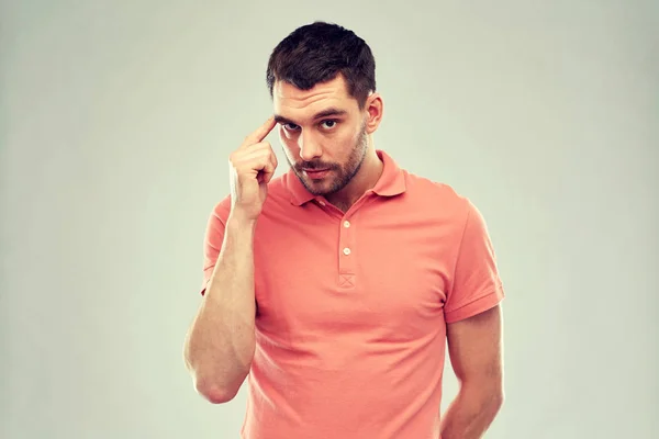 Mann mit Finger an der Schläfe vor grauem Hintergrund — Stockfoto