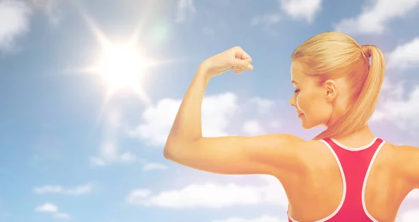 Счастливая спортивная женщина, показывающая бицепсы над небом и солнцем — стоковое фото