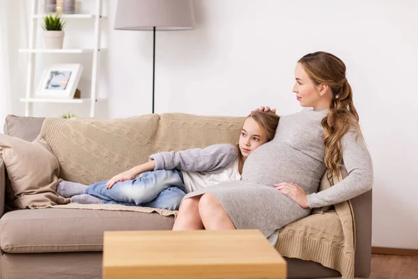 Счастливая беременная женщина и девочка на диване дома — стоковое фото