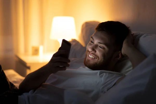 Gelukkig jongeman met smartphone in bed 's nachts — Stockfoto