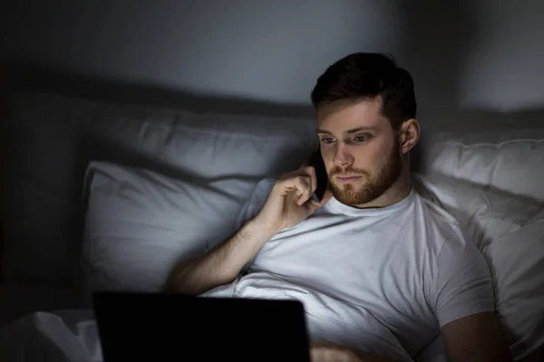 Hombre con portátil llamando en el teléfono inteligente por la noche —  Fotos de Stock