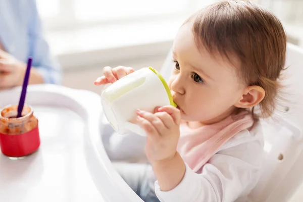 Bebé bebiendo de la taza de la boquilla en silla alta en casa — Foto de Stock