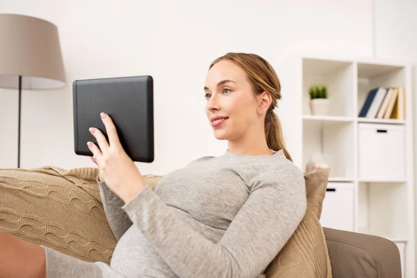 Glad gravid kvinna med tablett dator hemma Stockfoto