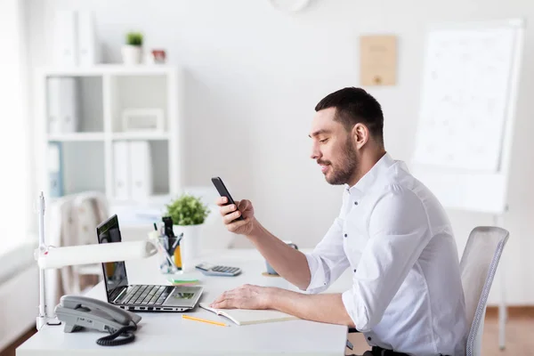 Empresário com smartphone e notebook no escritório — Fotografia de Stock