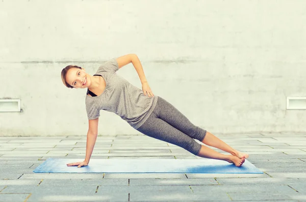 Vrouw maken yoga in zijkant plank pose op de mat — Stockfoto