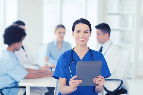 Happy doctor with tablet pc over team at clinic — Stock Photo, Image