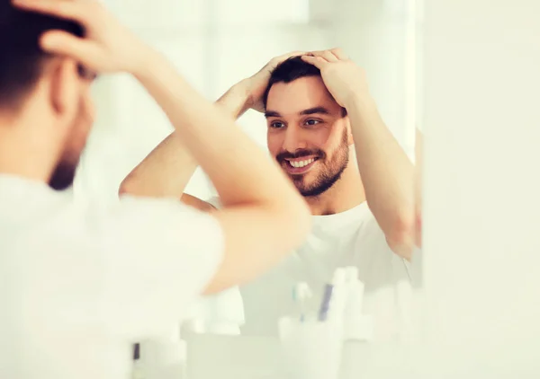 Glücklicher junger Mann schaut auf Spiegel im heimischen Badezimmer — Stockfoto