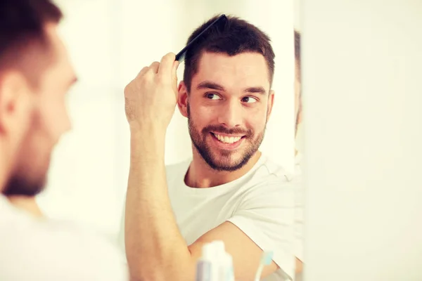 Homem feliz escovando o cabelo com pente no banheiro — Fotografia de Stock