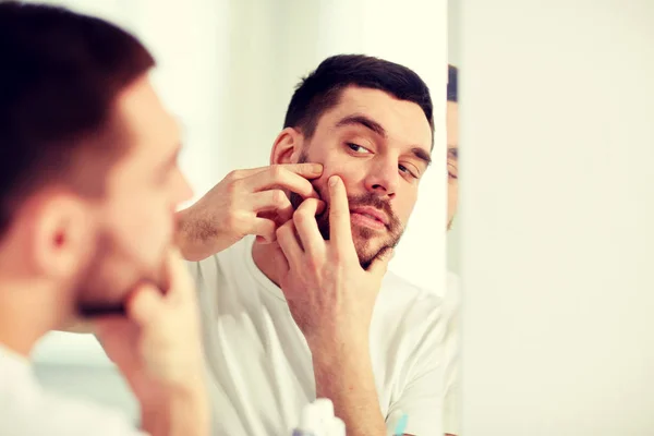 Man squeezing pimple at bathroom mirror — Stock Photo, Image