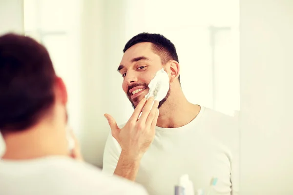 Hombre feliz aplicando espuma de afeitar en el espejo del baño — Foto de Stock