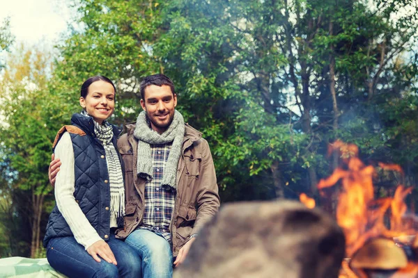 Feliz pareja sentada en el banco cerca del fuego del campamento —  Fotos de Stock