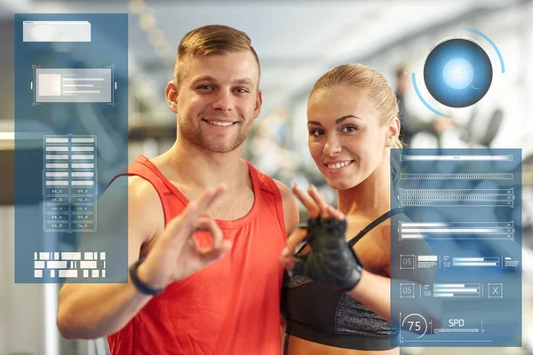 Sonriente hombre y mujer mostrando ok signo de mano en el gimnasio —  Fotos de Stock