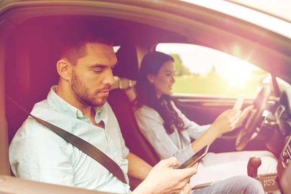 Man och kvinna med smartphones i bil — Stockfoto