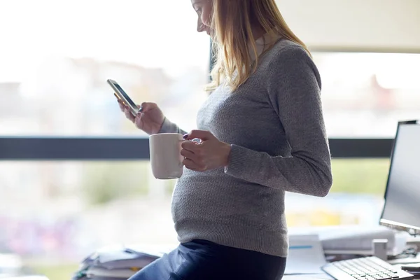 Femme d'affaires enceinte avec smartphone au bureau — Photo
