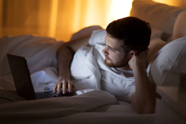 Jonge man met laptop in bed thuis slaapkamer — Stockfoto