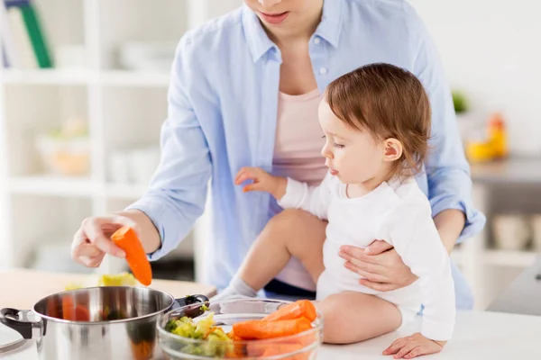 Mãe feliz e bebê cozinhar legumes em casa — Fotografia de Stock