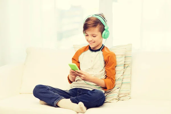 Niño feliz con teléfono inteligente y auriculares en casa —  Fotos de Stock