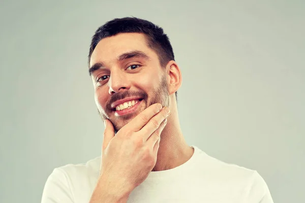 Счастливый молодой человек, трогающий лицо или бороду — стоковое фото