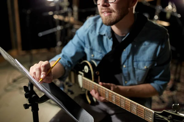 Uomo con chitarra iscritto a libro di musica in studio — Foto Stock