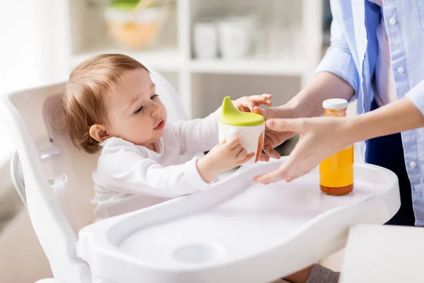 Mãe dando copo de bico com suco para bebê em casa — Fotografia de Stock