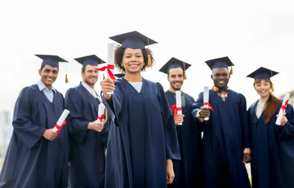 Glada studenter i murbruk styrelser med diplom — Stockfoto