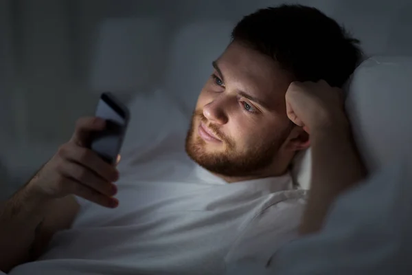年轻人，晚上在床上拿着智能手机 — 图库照片