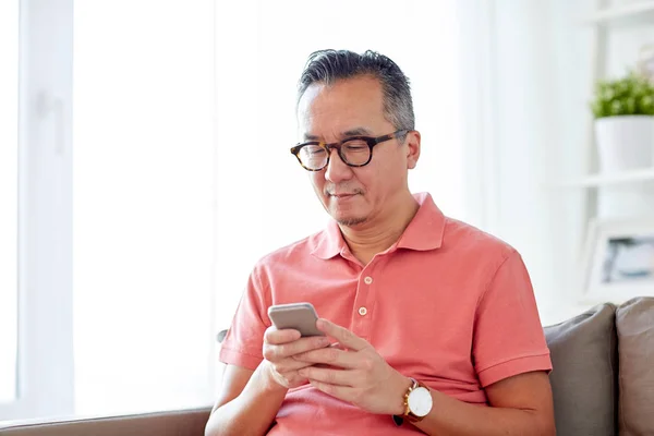 Homem com smartphone sentado no sofá em casa — Fotografia de Stock