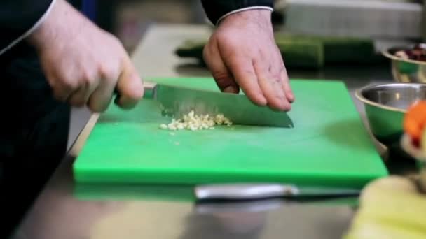 Руки чоловічого шеф-кухаря готують подрібнення часнику на кухні — стокове відео