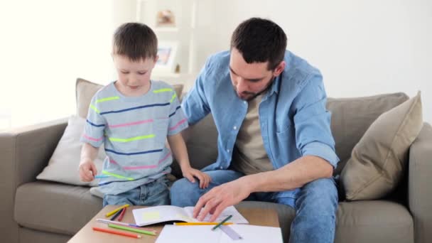Отец и маленький сын с карандашами рисуют дома — стоковое видео