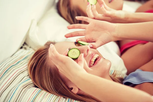 Mujeres jóvenes felices con máscara de pepino acostado en la cama — Foto de Stock