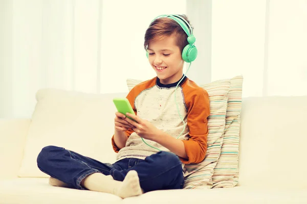 Niño feliz con teléfono inteligente y auriculares en casa —  Fotos de Stock