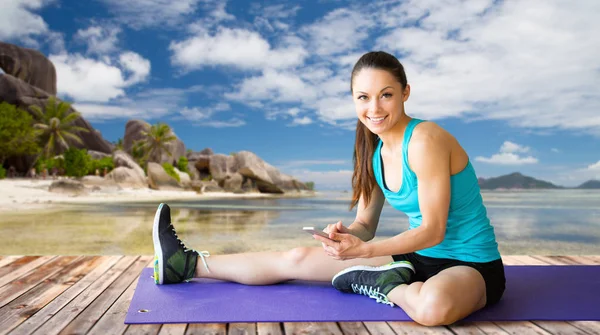 Happy woman with smartphone stretching leg on mat — Stock Photo, Image