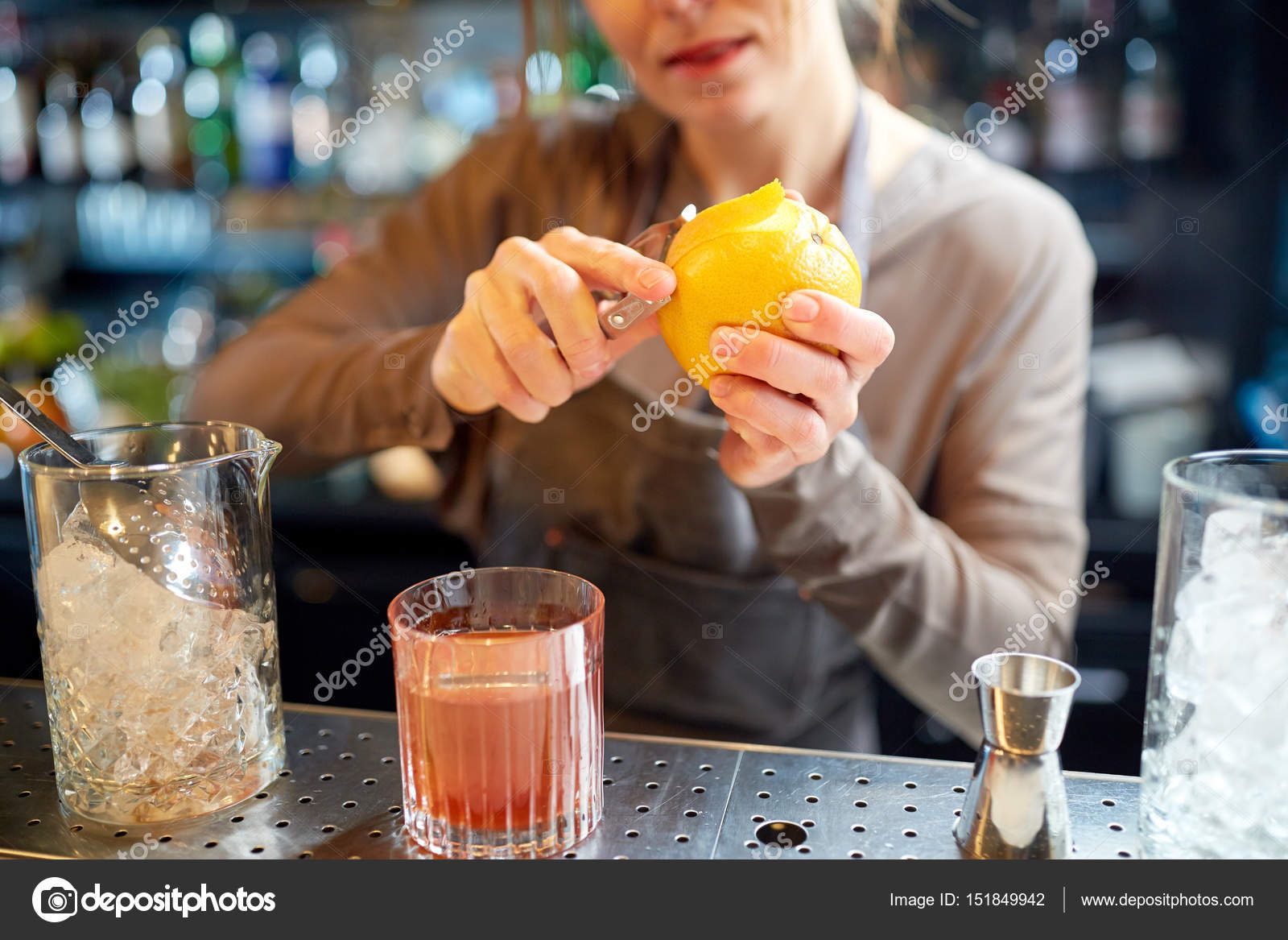 Bartender peels orange peel for cocktail at bar Stock Photo by
