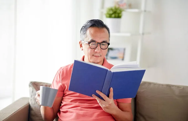 Człowiek siedzi na kanapie i czytanie książki w domu — Zdjęcie stockowe