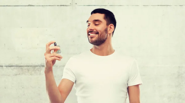 Hombre sonriente con perfume masculino sobre fondo gris — Foto de Stock