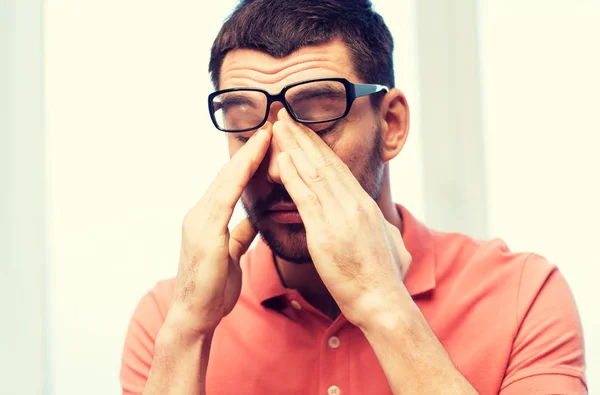 Hombre cansado en anteojos frotando los ojos en casa —  Fotos de Stock