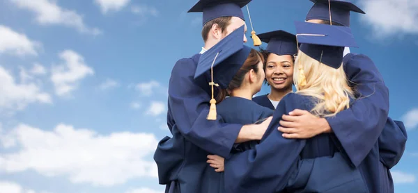 Happy students or bachelors hugging over blue sky — Stock Photo, Image