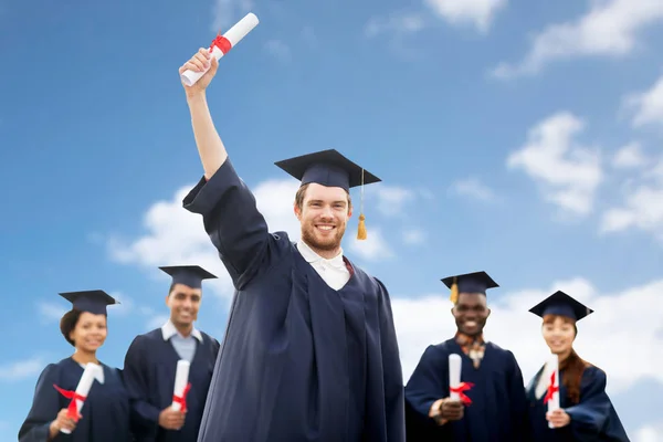 Studenti nebo staří mládenci s diplomy nad modrá obloha — Stock fotografie