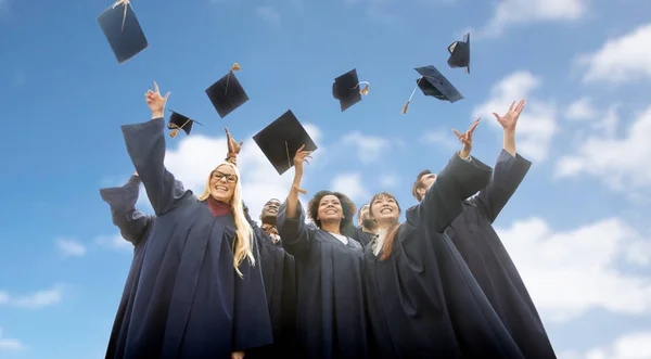 Happy students throwing mortar boards up — Stock Photo, Image