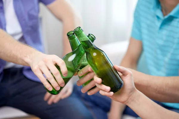 Close up of friends clinking beer bottles at home — Stock Photo, Image