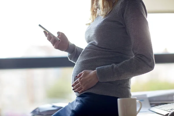 Mujer de negocios embarazada con teléfono inteligente en la oficina — Foto de Stock