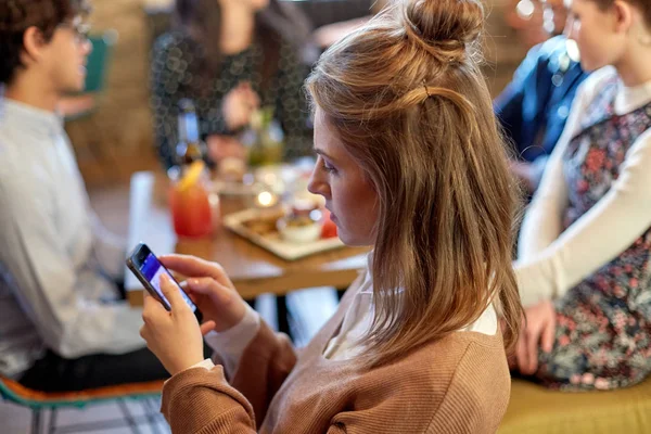 Mulher com smartphone e amigos no restaurante — Fotografia de Stock