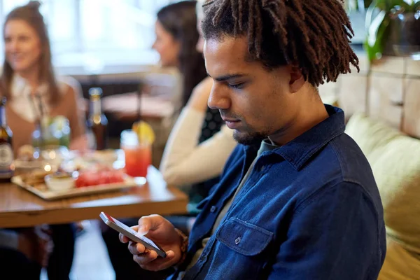 Homem com smartphone e amigos no restaurante — Fotografia de Stock