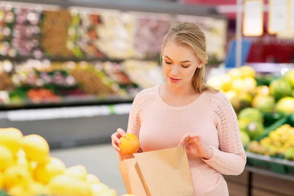 Беременная женщина с сумкой покупает апельсины в магазине — стоковое фото