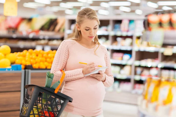 Pregnant woman with shopping basket at grocery — Stock Photo, Image