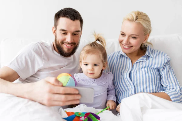 Familia feliz con teléfono inteligente en la cama en casa —  Fotos de Stock