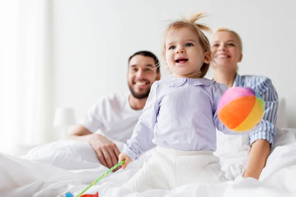 Enfant heureux avec des jouets et des parents au lit à la maison — Photo