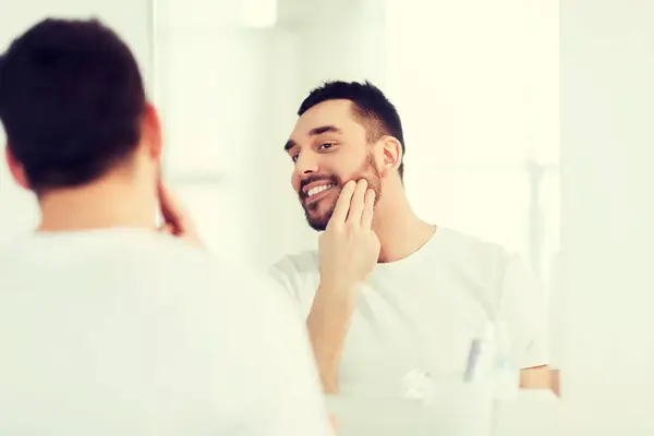 Happy young man applying cream to face at bathroom — Stock Photo, Image