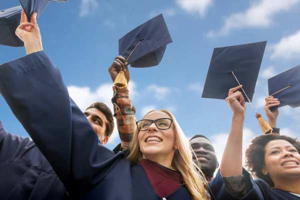 Gelukkig vrijgezellen zwaaien mortierplanken boven de hemel — Stockfoto